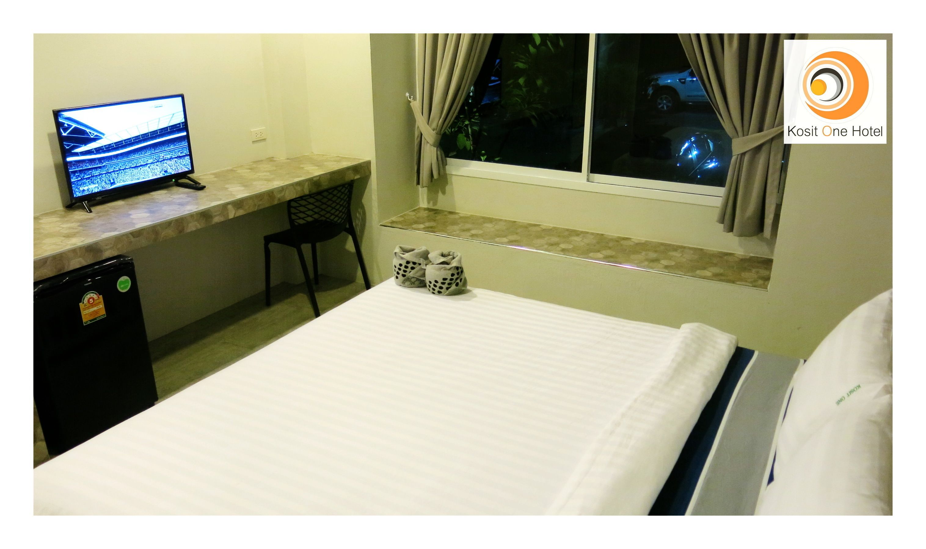 A hotel room with a bed, a desk with a computer, a chair, and a small refrigerator.
