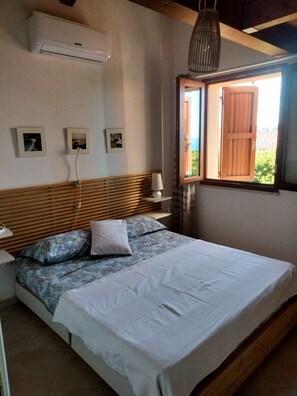 A bedroom with a bed, a bedside table, a lamp, and a window with wooden shutters. - Wonderful view of the sea. Romantic and relaxing place suitable for a couple. (Sassari)
