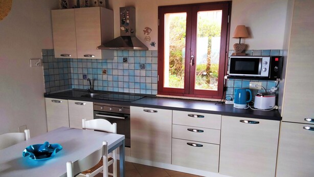 Une cuisine avec un mur recouvert de carreaux, un four à micro-ondes, un grille-pain et une fenêtre donnant sur un paysage verdoyant.