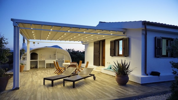 A modern outdoor patio with wooden lounge chairs, a covered seating area, and a potted plant.