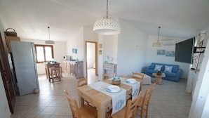 A spacious living area with a dining table set for four, a blue sofa, and a television mounted on the wall.