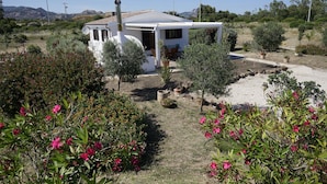 A white house with a patio, surrounded by various plants and flowers.