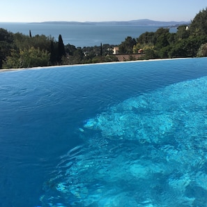 A clear blue pool with a view of the sea and distant hills.