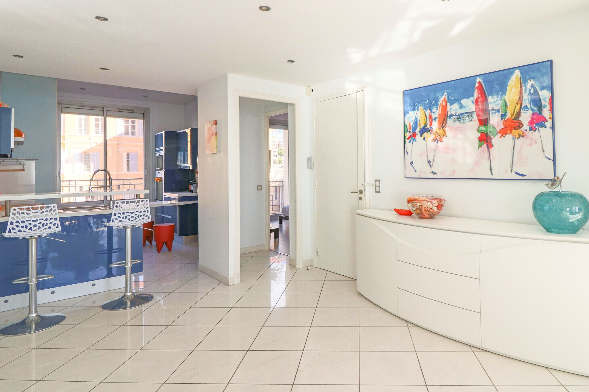 A modern kitchen with a blue island, white cabinets, and a large window.