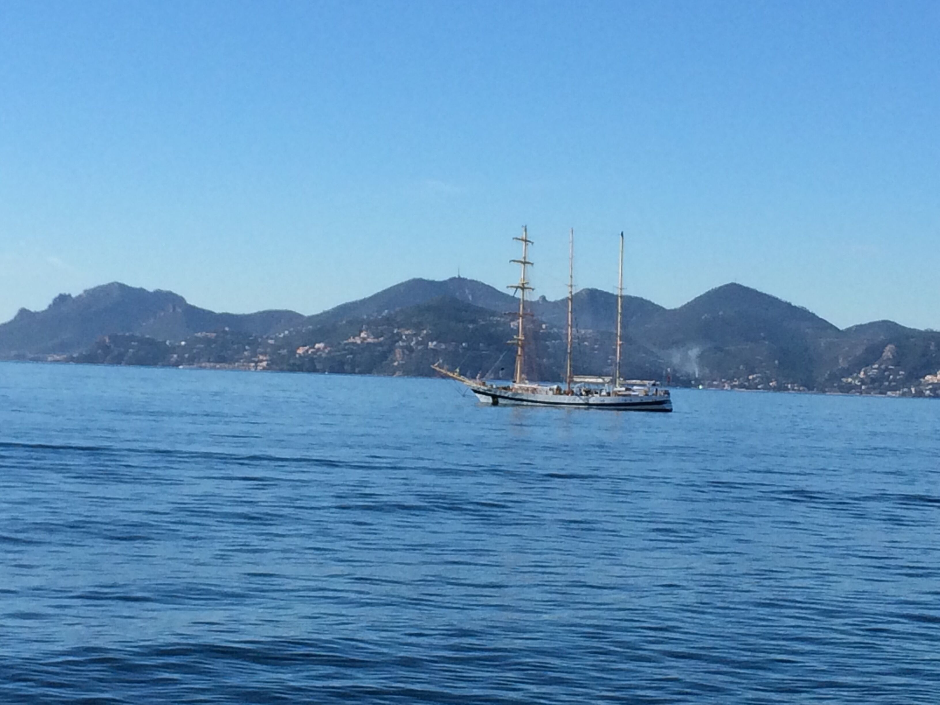 A sailboat on a calm sea with a mountainous coastline in the background.