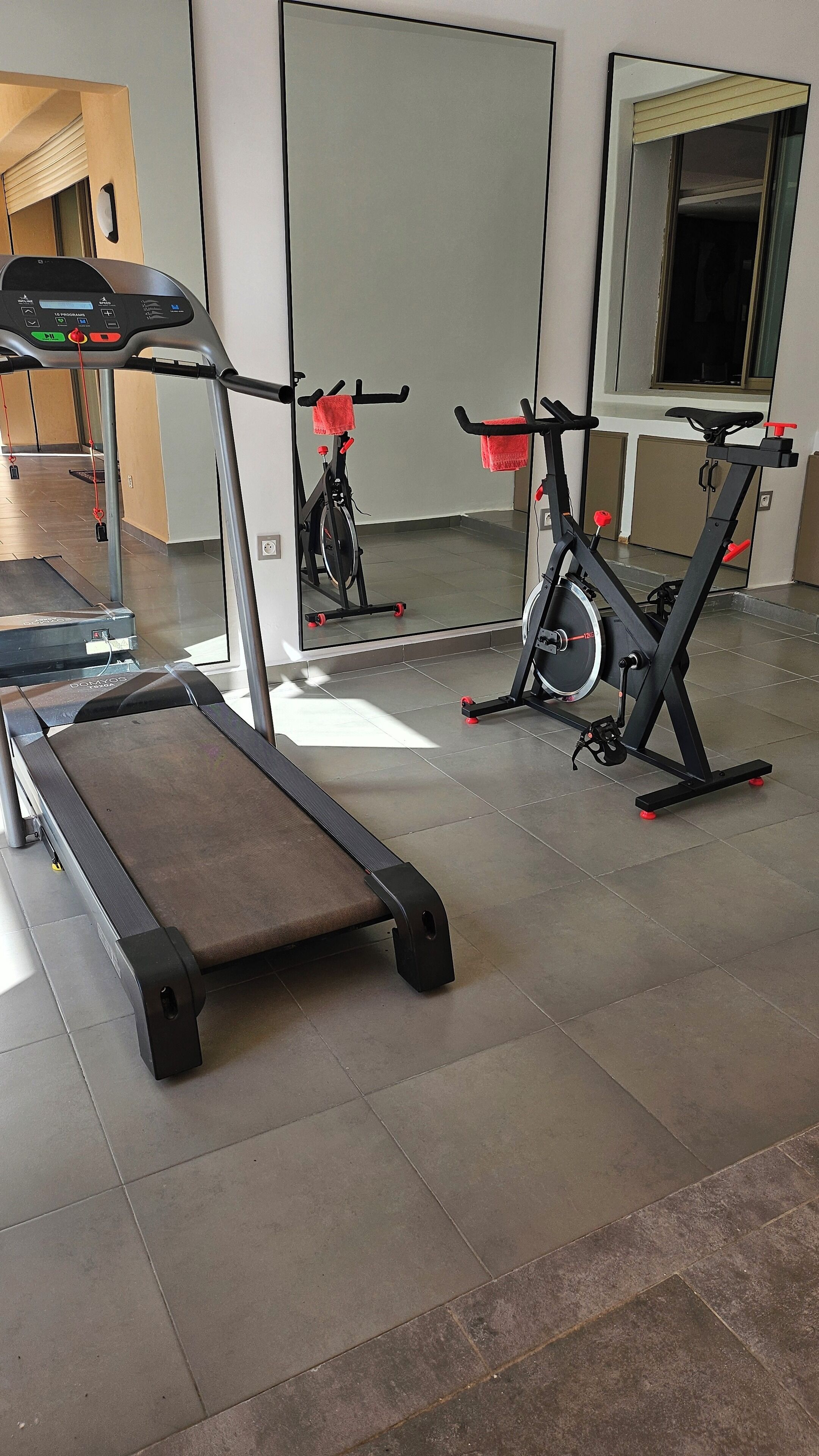 Ein Fitnessraum mit Cardiogeräten, darunter Laufbänder und Ergometer, sowie einer Spiegelwand.