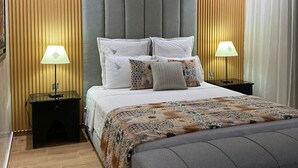 Ein modernes Schlafzimmer mit einem großen Bett, zwei Nachttischen mit Lampen, einem Kopfteil mit vertikalen Paneelen und einer gemusterten Bettdecke.