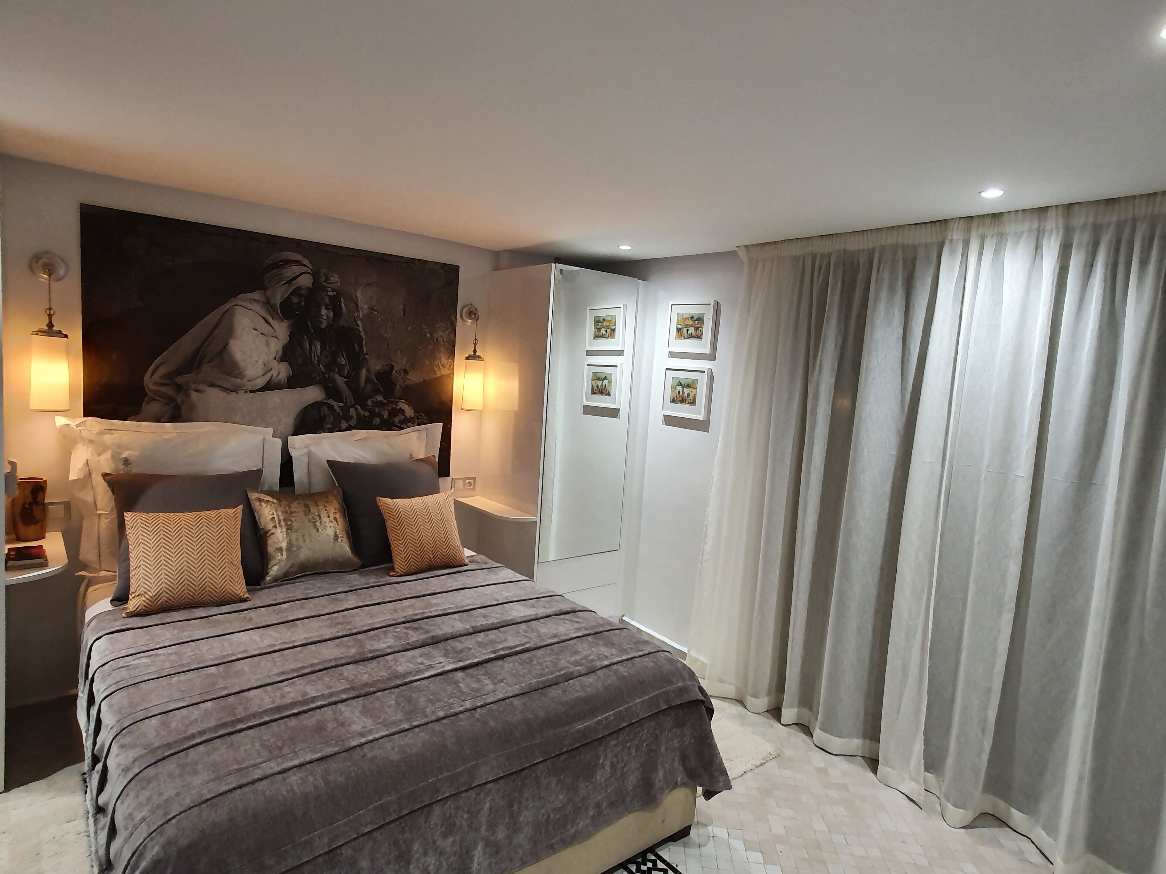 Quarto com cama grande, cabeceira com pintura, luminárias de mesa e um guarda-roupa.