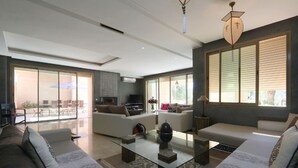 Ein geräumiges Wohnzimmer mit Kamin, großen Fenstern und einer modernen Deckenleuchte.