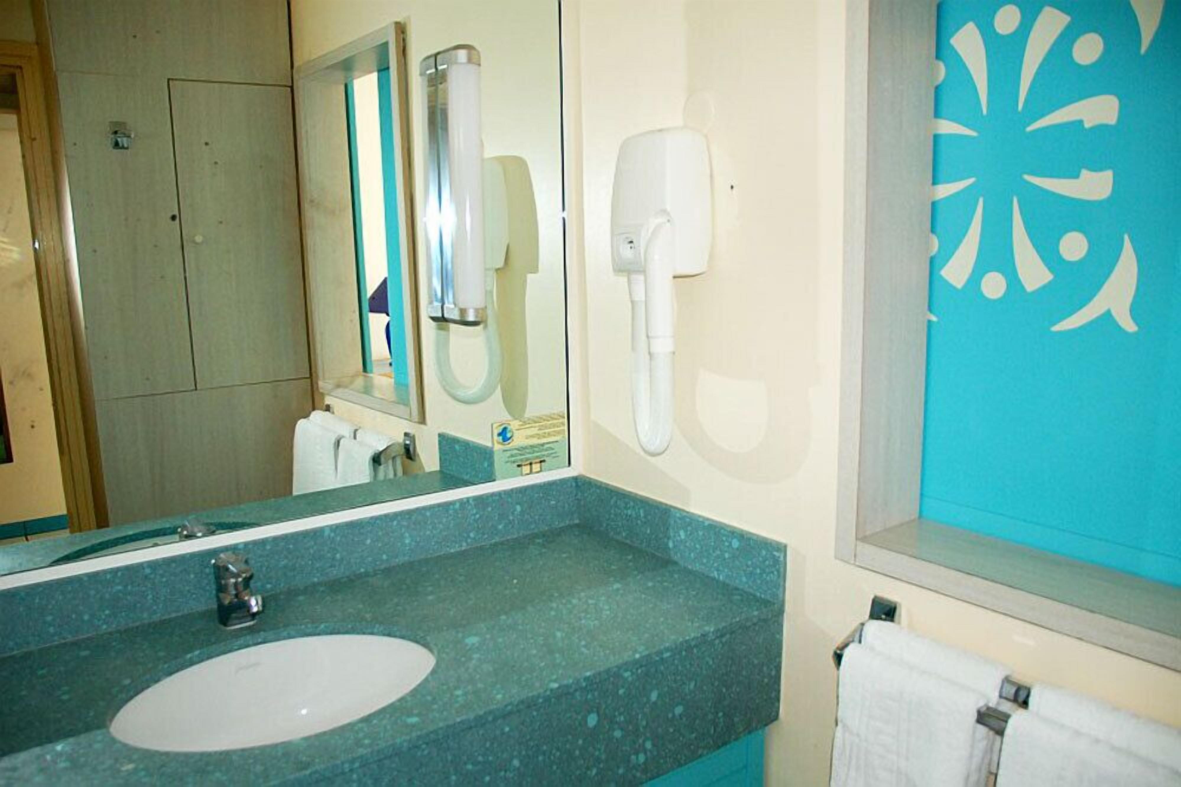 A bathroom with a sink, mirror, towel rack, and a wall-mounted hairdryer.