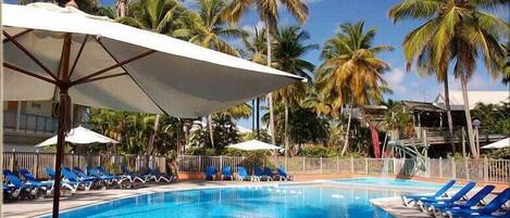 Una piscina con acqua azzurra, circondata da palme e sdraio blu.