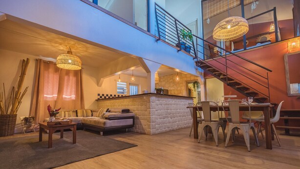 A spacious living area with a sofa, dining table, and chairs, a staircase, and a balcony with a railing and plants. - Villa Noja***** HEATED POOL, beaches, volcano, hiking, Trail... (Saint Louis)