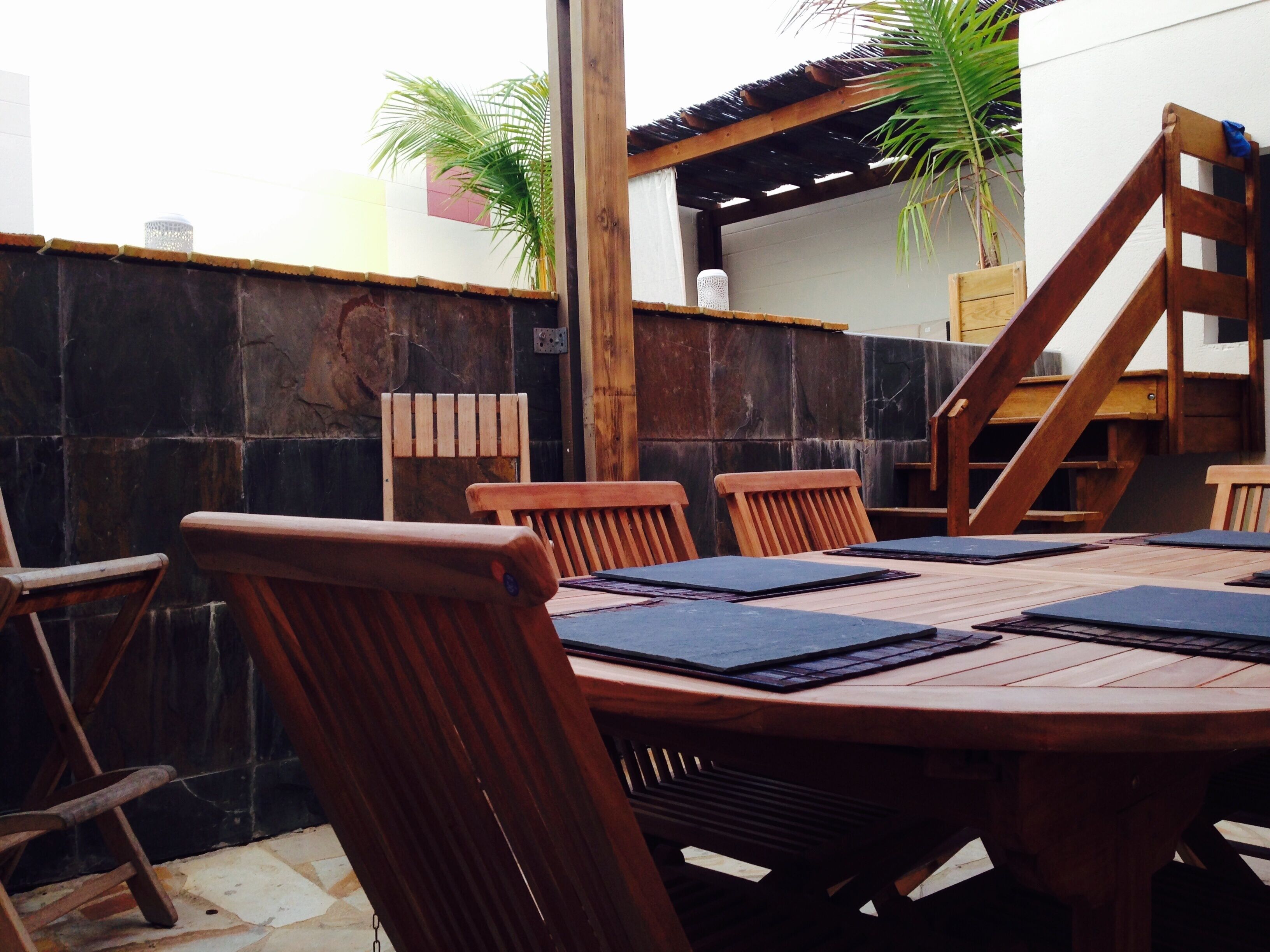 A wooden dining table with chairs, a wooden staircase, and a tiled wall.