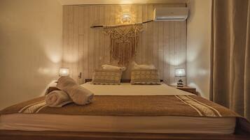 A bedroom with a wooden headboard, two bedside tables with lamps, a bed with a brown blanket and pillows, and a wall-mounted air conditioner.