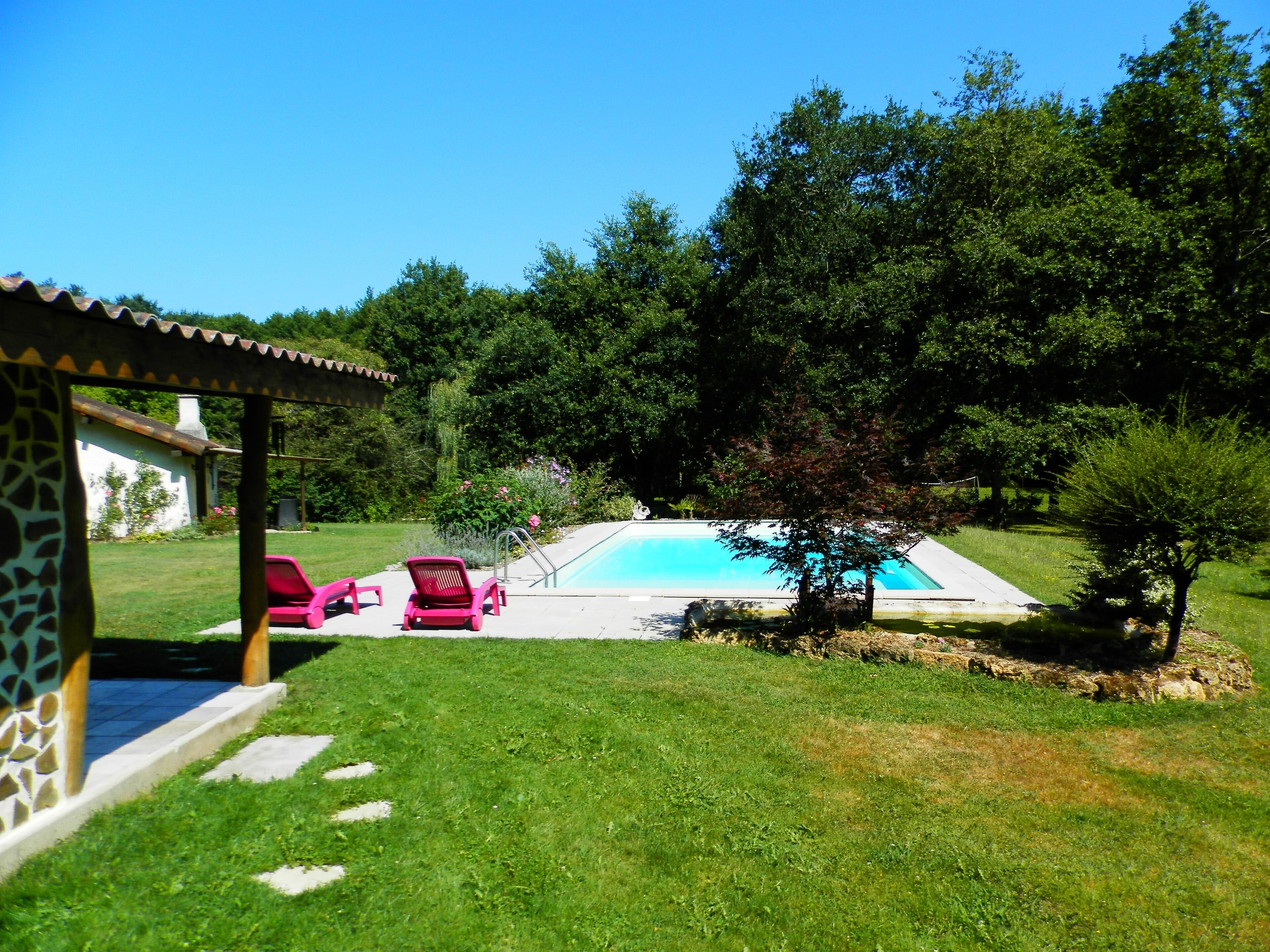 Una piscina con una piccola zona solarium, circondata da un prato curato e alberi.