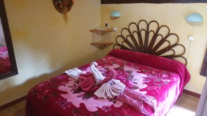 Una cama con colcha floral y dos toallas, cabecera de madera y dos lámparas de pared.