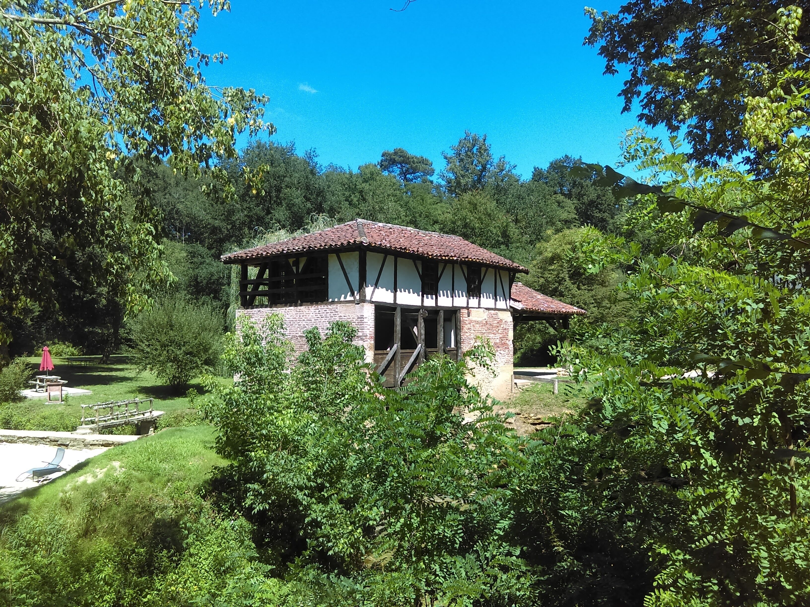 A rustic building with a tiled roof, surrounded by lush greenery.