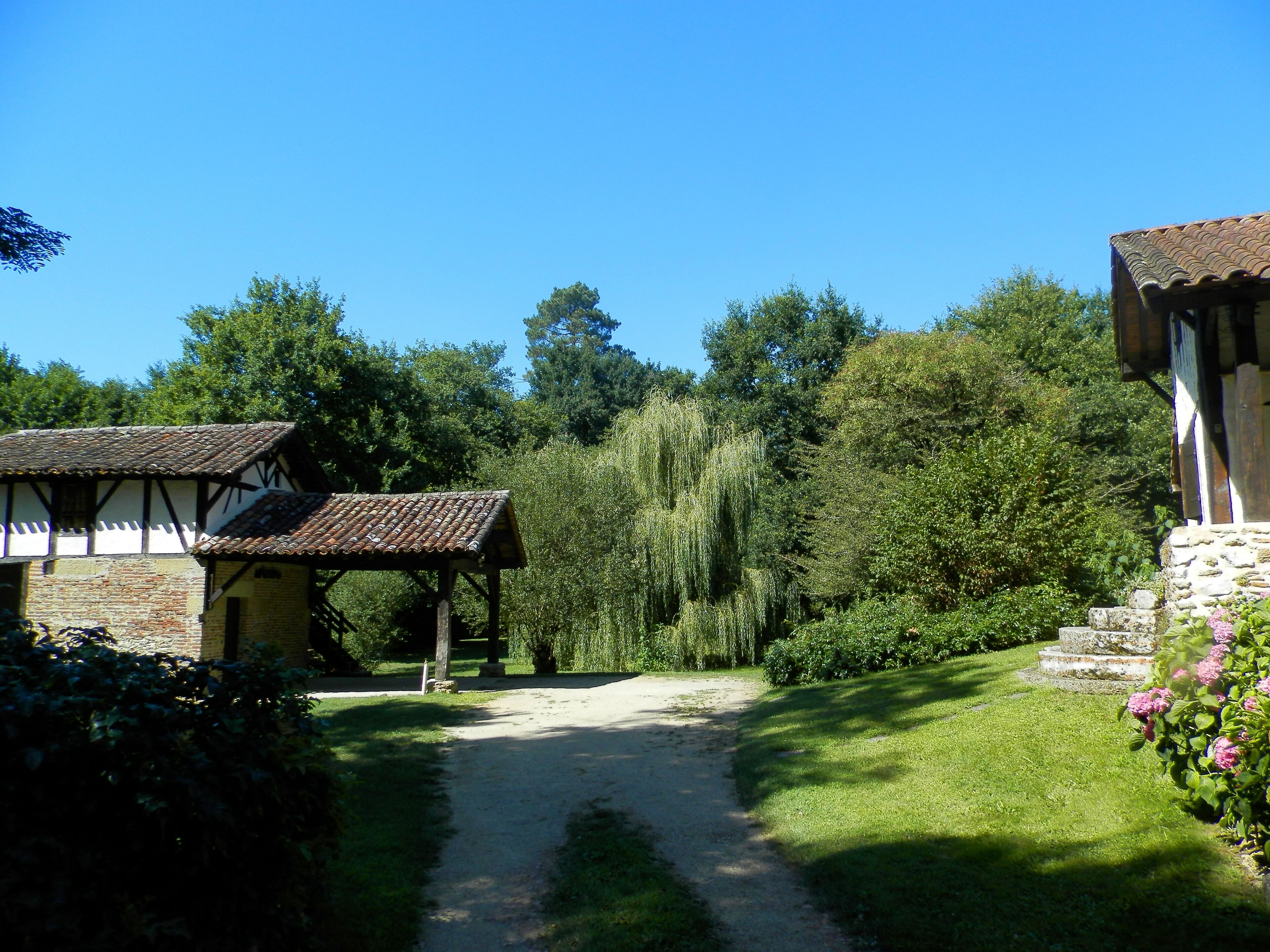 A traditional building with a tiled roof and stone walls, surrounded by lush greenery and a clear path leading to it.