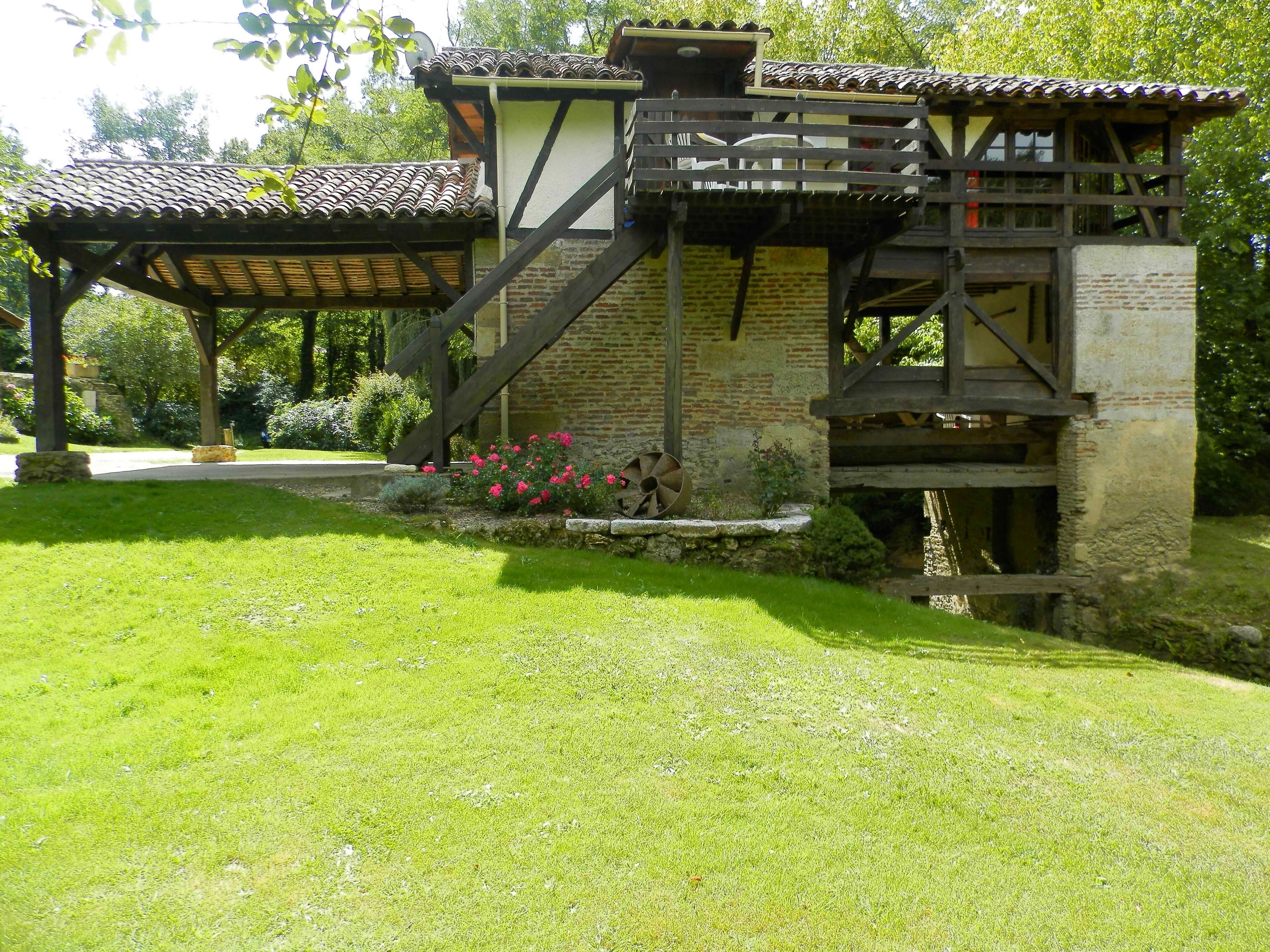 Il s’agit d’un bâtiment traditionnel doté d’un escalier en bois menant à un balcon, lequel est entouré d’un jardin bien entretenu, avec de la pelouse et des fleurs.