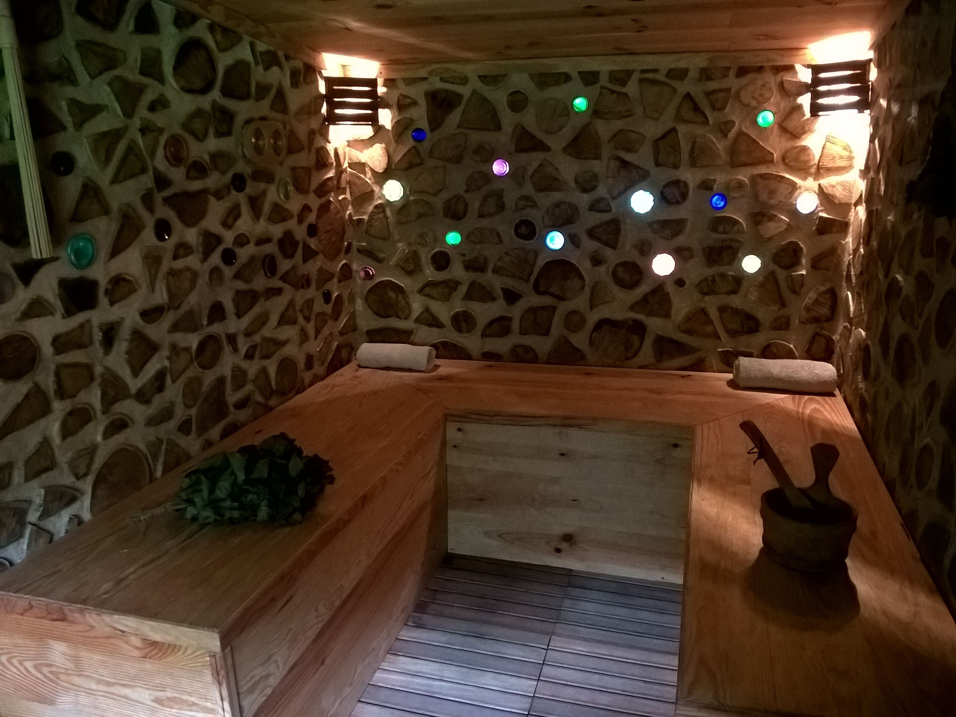 Ein Zimmer mit Steinwänden, einer Holzbänke, einem kleinen Tisch und einer Bank mit Handtuch.