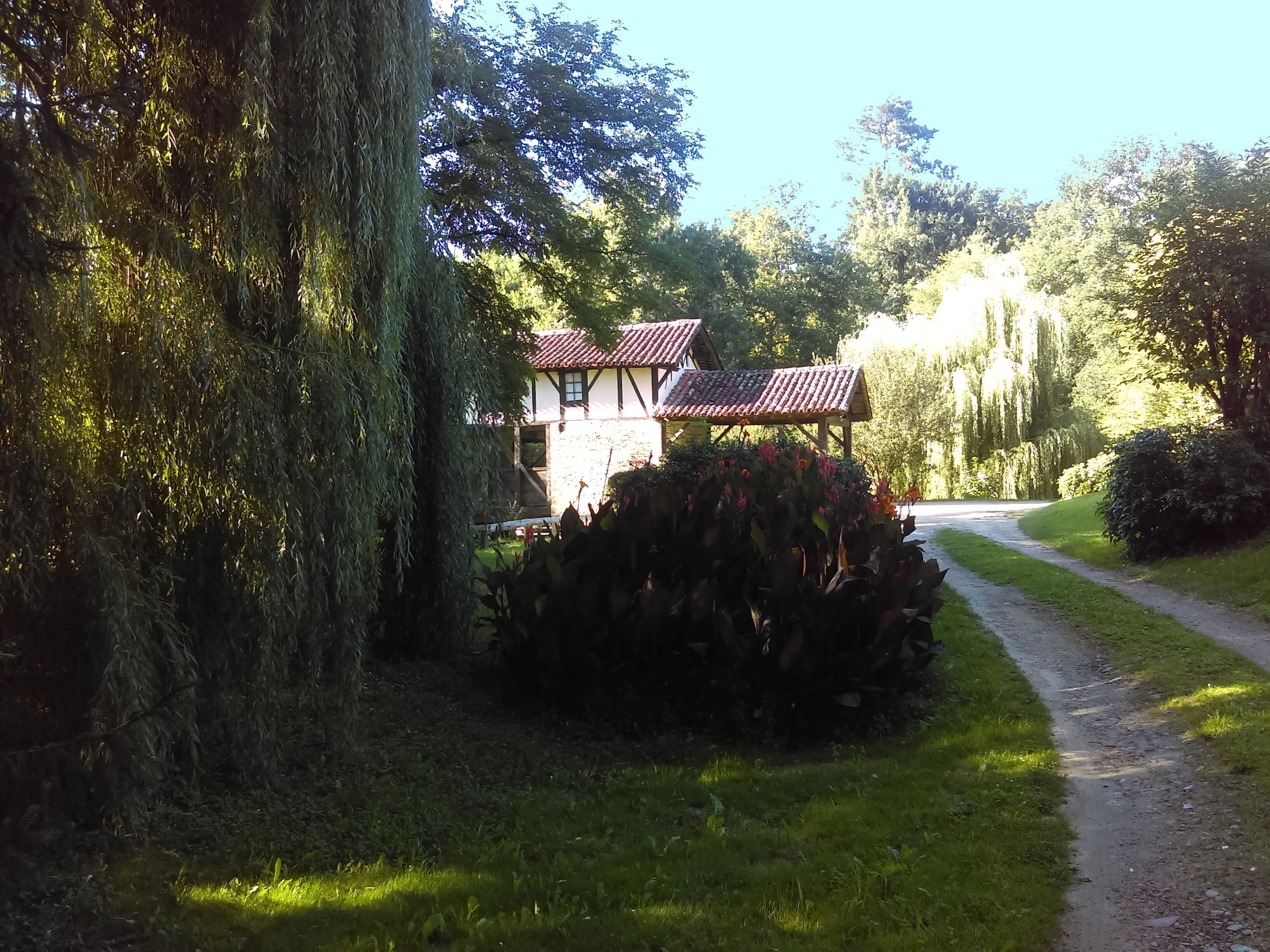 A traditional building with a tiled roof, surrounded by lush greenery and a gravel path.