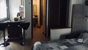 Ein modernes Hotelzimmer mit einem Bett, einem Schreibtisch mit Stuhl, einem Kleiderschrank und einem durchgegangene Tür erkennbaren Badezimmer.