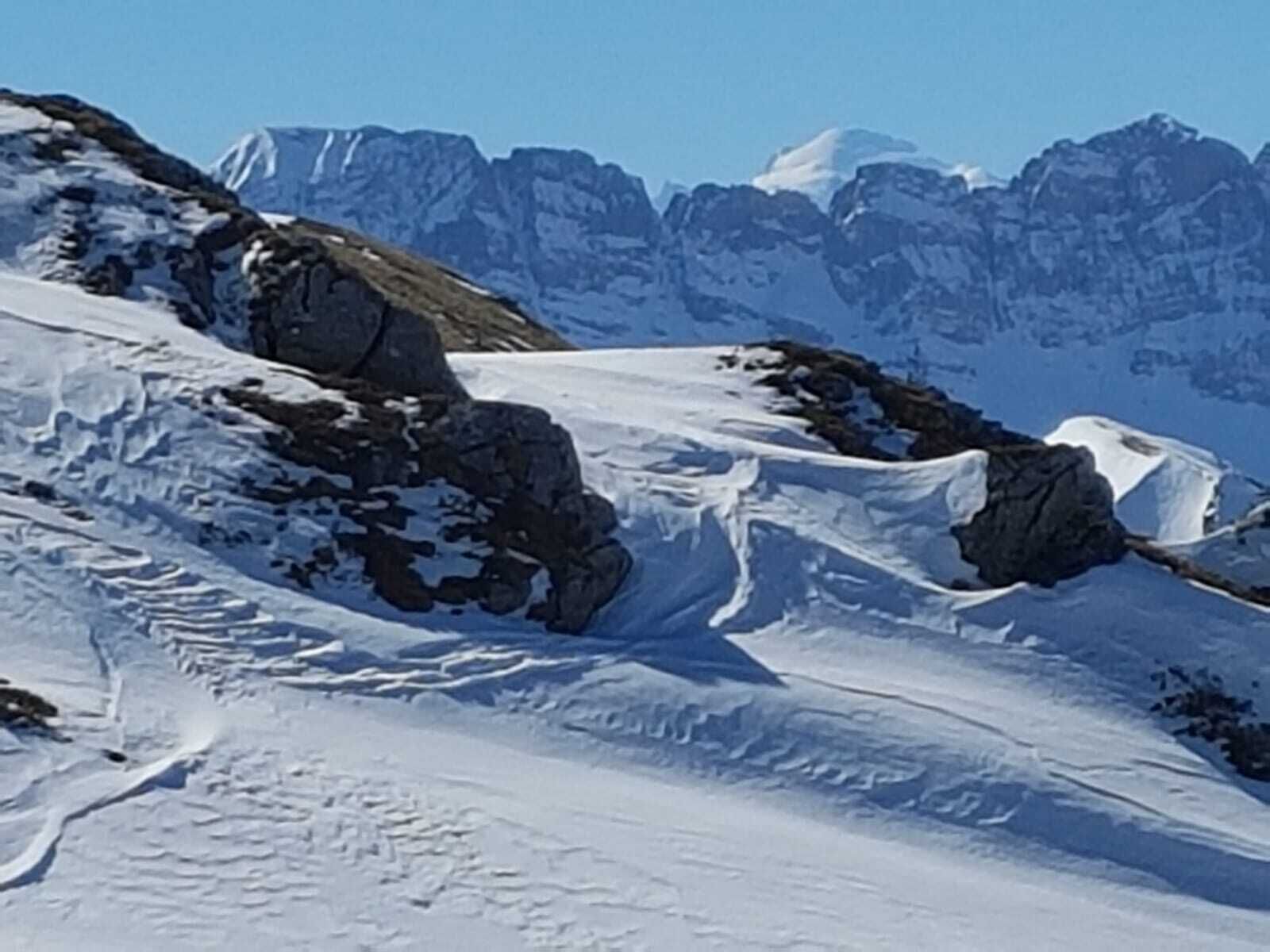 A snow-covered mountain landscape with rocky outcrops and a clear sky.