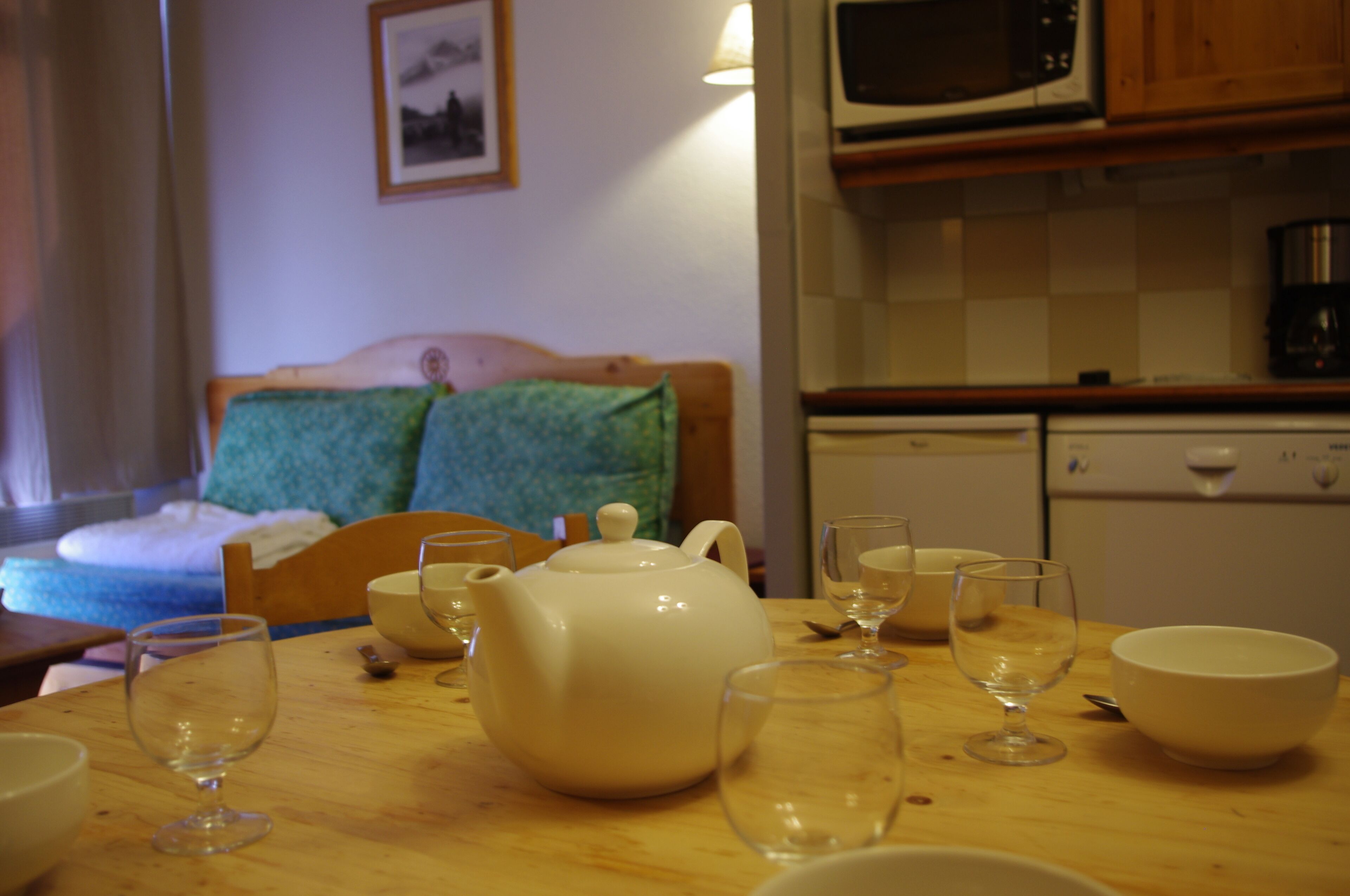 A kitchen area with a microwave, coffee maker, and a wooden table with a teapot and glasses.
