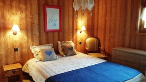 Une pièce aux murs lambrés, comprenant un lit, deux lampes de chevet, une chaise et une commode.