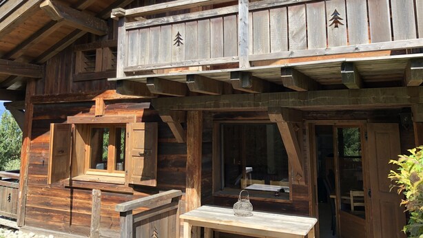 A wooden cabin with a balcony, large windows, and a small table with a lantern.