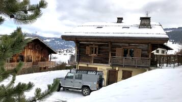 Eine Holzhütte mit Balkon, ein geparktes Fahrzeug und eine verschneite Landschaft mit Bergen im Hintergrund.