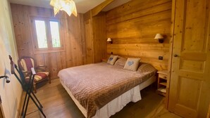A wooden room with a bed, two wall lamps, a window, and a chair.