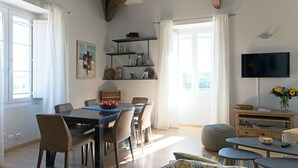 A dining area with a table and chairs, a TV on the wall, and a bookshelf with various items. - The bright and colorful Duplex Mill in Saint-Rémy-de-Provence (Saint-Rémy-De-Provence)