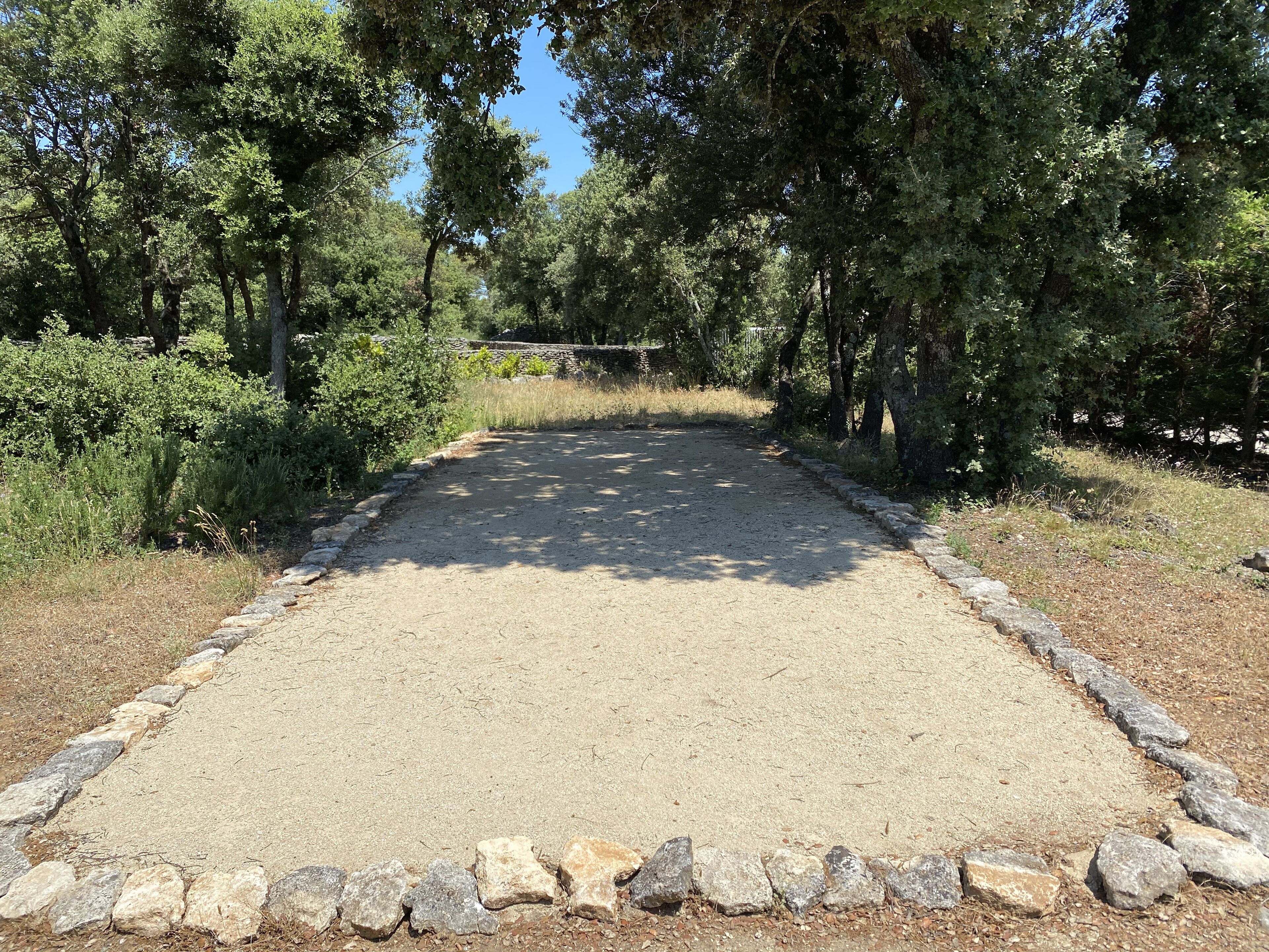 A gravel path bordered by stone edging, surrounded by dense trees and shrubs.