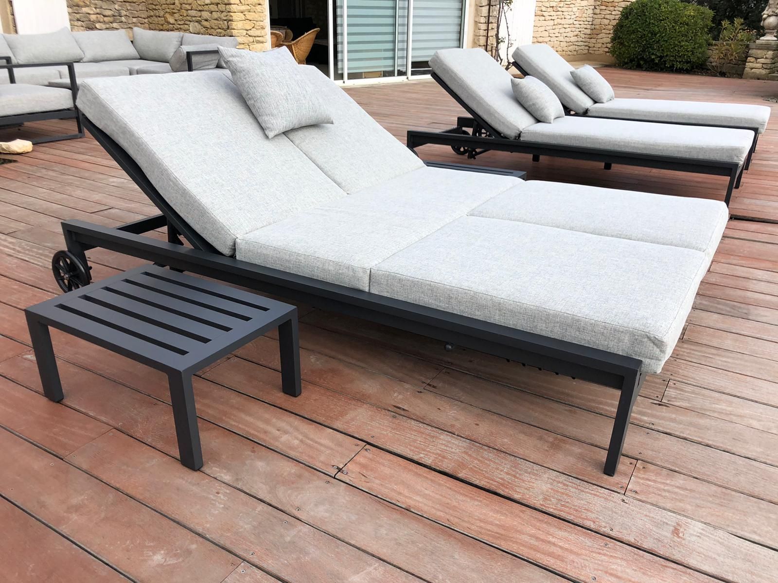 A sun lounger with a small table in front, set on a wooden deck.