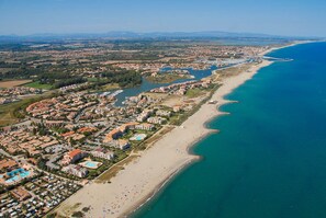 An aerial view of a coastal resort with beachfront properties, a marina, and a beach with umbrellas.