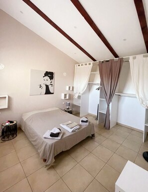 A hotel room with a bed, bedside tables, a nightstand, a wall-mounted artwork, a wardrobe, and a window with curtains.