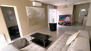 Una sala de estar moderna con un sofá grande de color gris, una mesa de centro negra y un televisor al fondo.