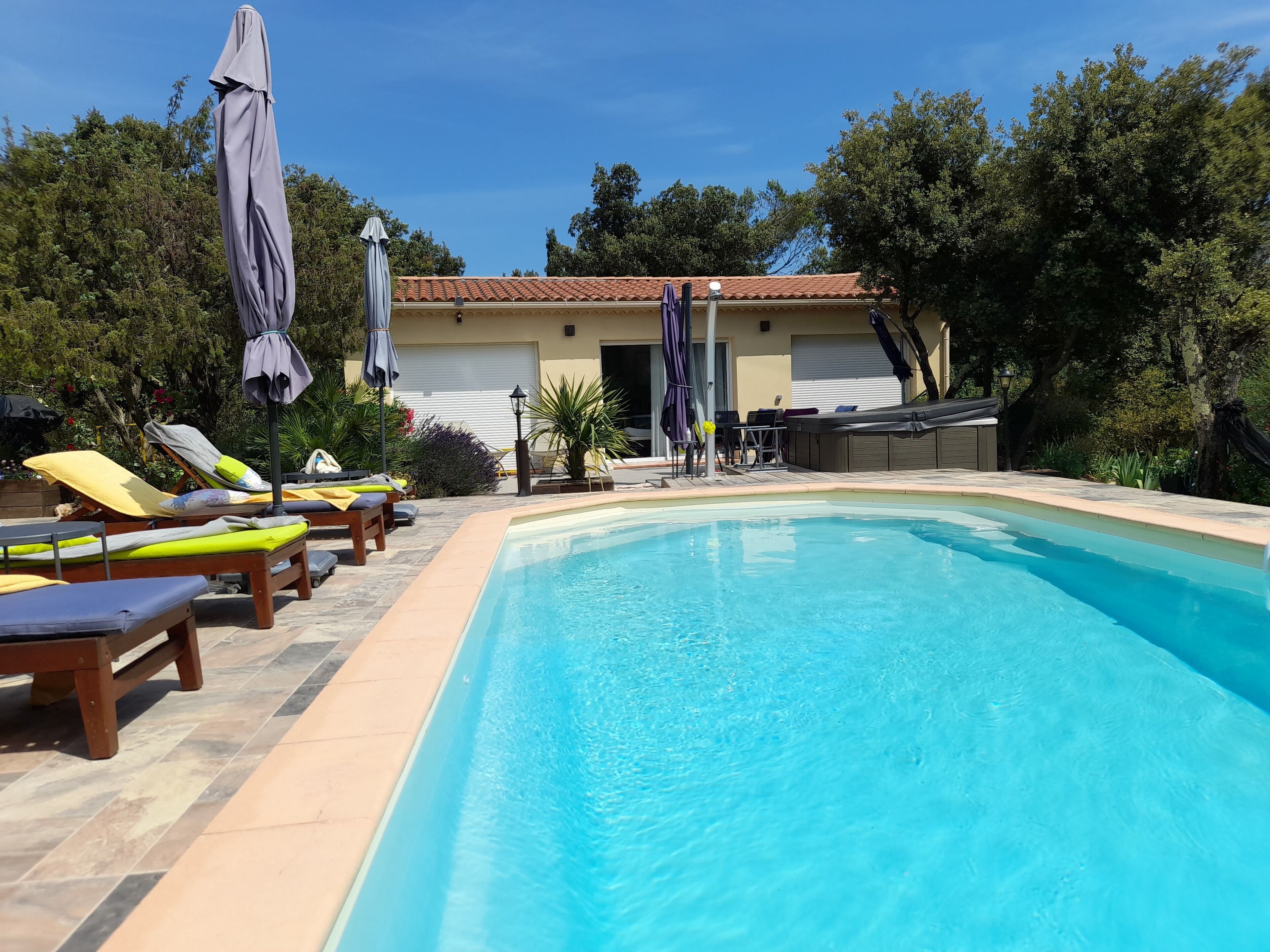 Ein Swimmingpool mit Liegestühlen und Sonnenschirmen, umgeben von viel Grün und einem Gebäude mit Ziegeldach.