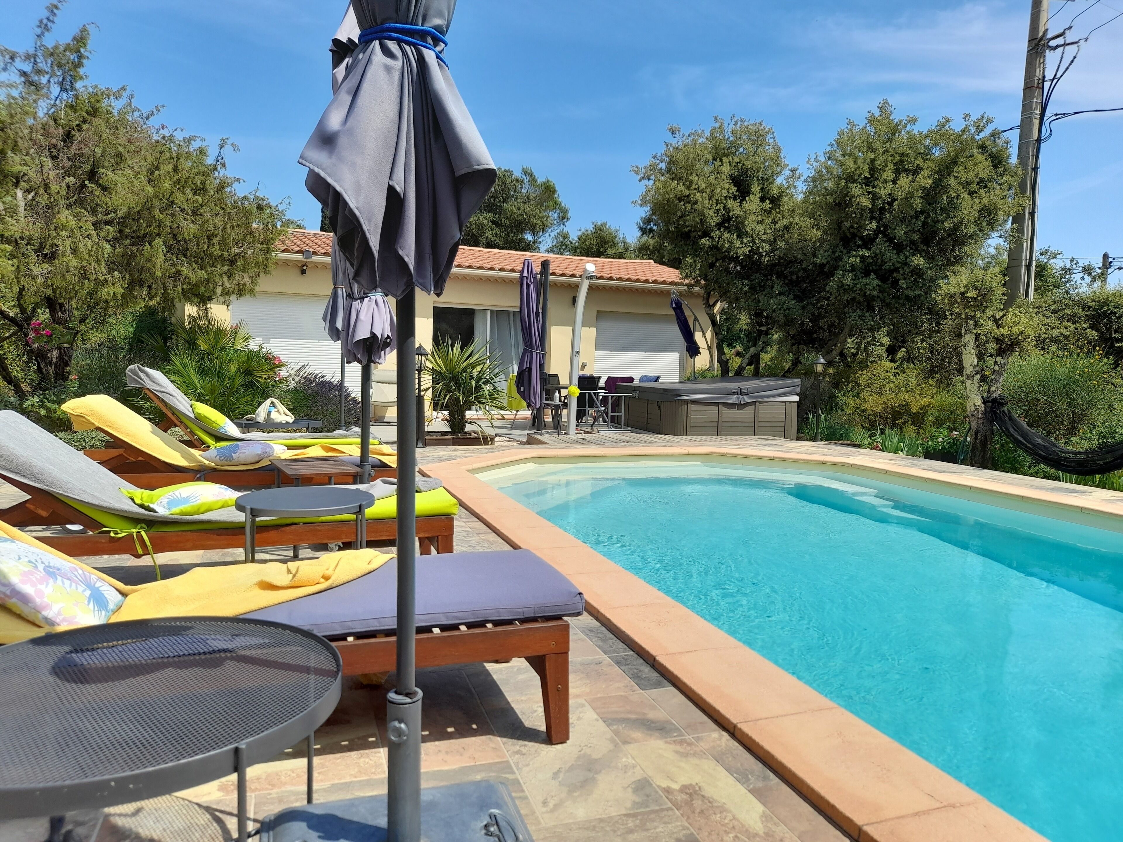 Un espace aménagé au bord de la piscine, avec des chaises longues et des parasols, un jacuzzi et un bâtiment en arrière-plan.