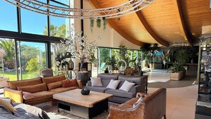 A spacious living area with multiple seating options, large windows offering views of the outdoors, and a variety of indoor plants. - VILLA DU SIECK 5* 14 p PISCINE int chau/securise Vue MER PLAGE SURF GR34 🏄‍♂️🏖 (Santec)