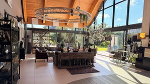 A spacious living area with a high wooden ceiling, large windows, and a central wooden coffee table surrounded by comfortable seating. - VILLA DU SIECK 5* 14 p PISCINE int chau/securise Vue MER PLAGE SURF GR34 🏄‍♂️🏖 (Santec)