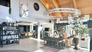 A spacious living area with a high ceiling, a central chandelier, and a variety of decorative items on shelves and tables. - VILLA DU SIECK 5* 14 p PISCINE int chau/securise Vue MER PLAGE SURF GR34 🏄‍♂️🏖 (Santec)