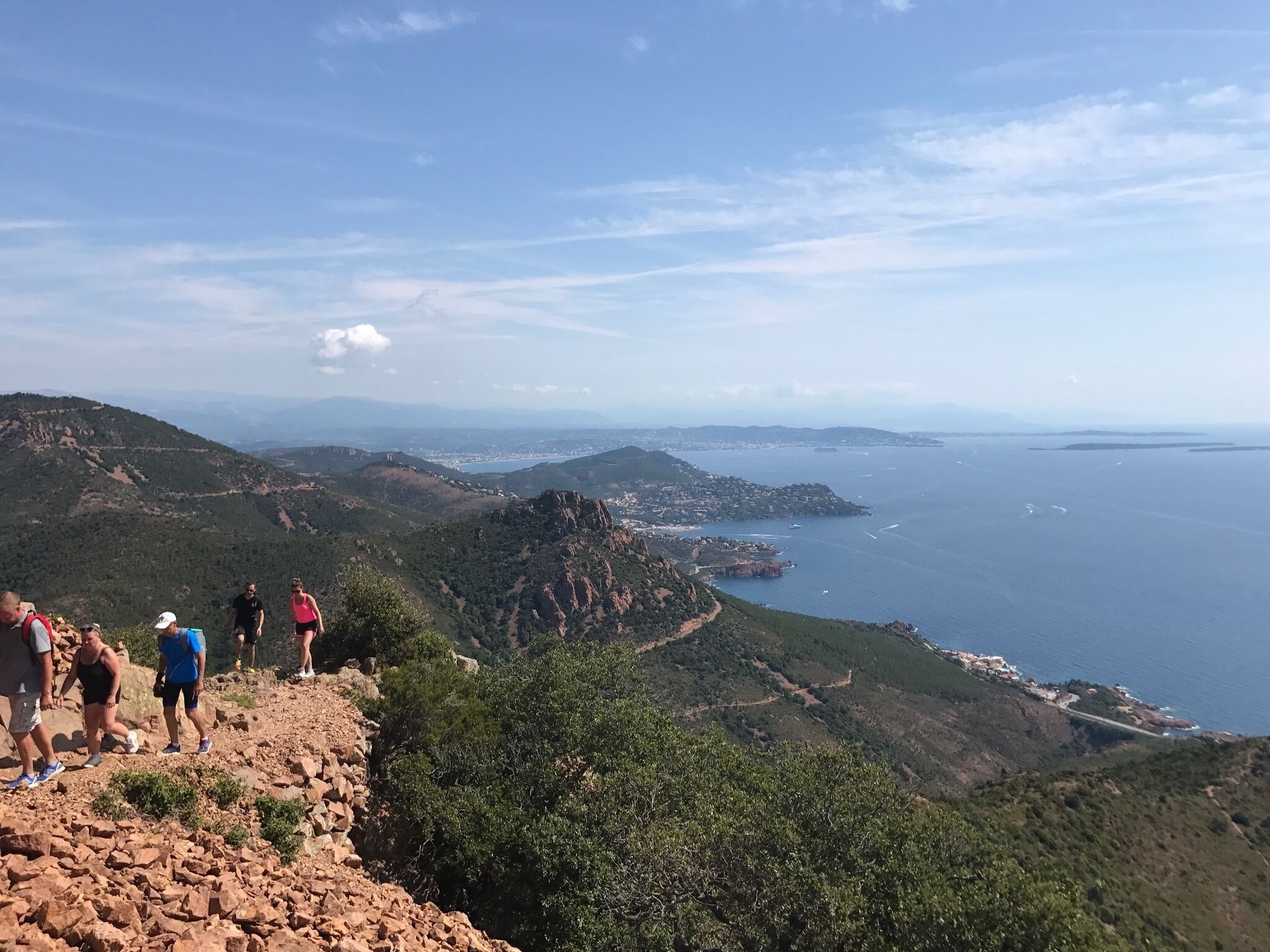 A group of people on a rocky hillside overlooking a coastal landscape with a view of the sea and distant islands.
