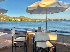 Une table installée sur la plage, avec un parasol blanc, une chaise et une bouteille d’eau.