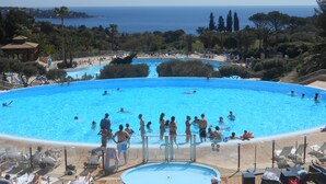 Una gran piscina al aire libre con múltiples carriles, rodeada de sillones de descanso y vistas al mar.