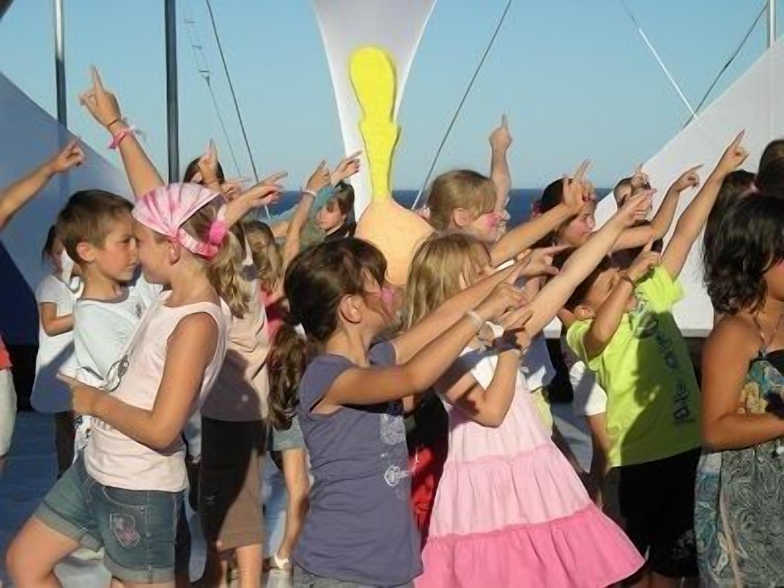 Un groupe d’enfants se trouve à l’extérieur, certains portent des chapeaux et d’autres ont les mains levées.