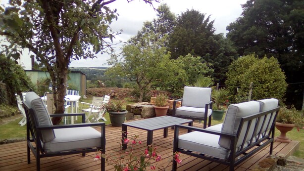 Una terraza exterior con una mesa y cuatro sillas, rodeada de plantas en macetas y árboles.