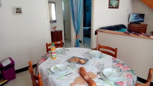 Comedor con una mesa redonda dispuesta para cuatro personas, mantel con motivos florales, platos, cubiertos y una baguette.