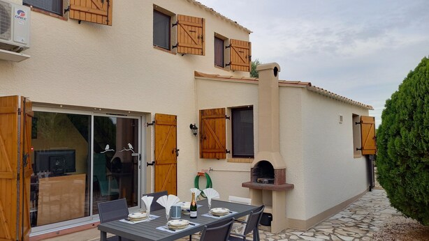 Un patio exterior con una mesa lista para comer, un horno de pizza y un ventanal corredero que da a una cocina.